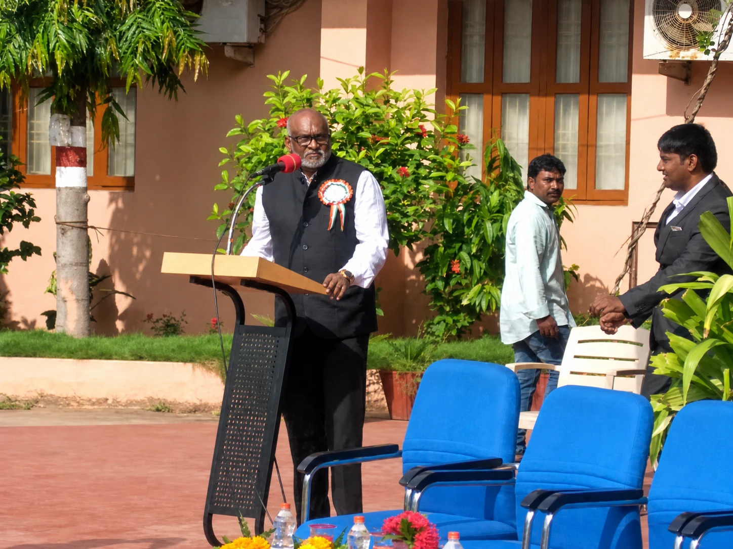 A speaker addressing an outdoor community gathering from a podium