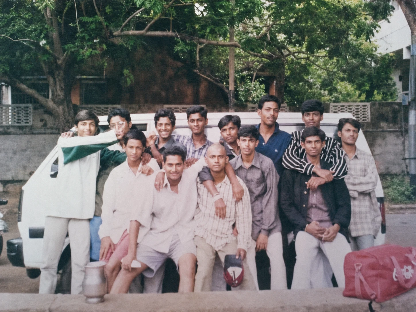 A young cricket team posing together beside their equipment near the ground